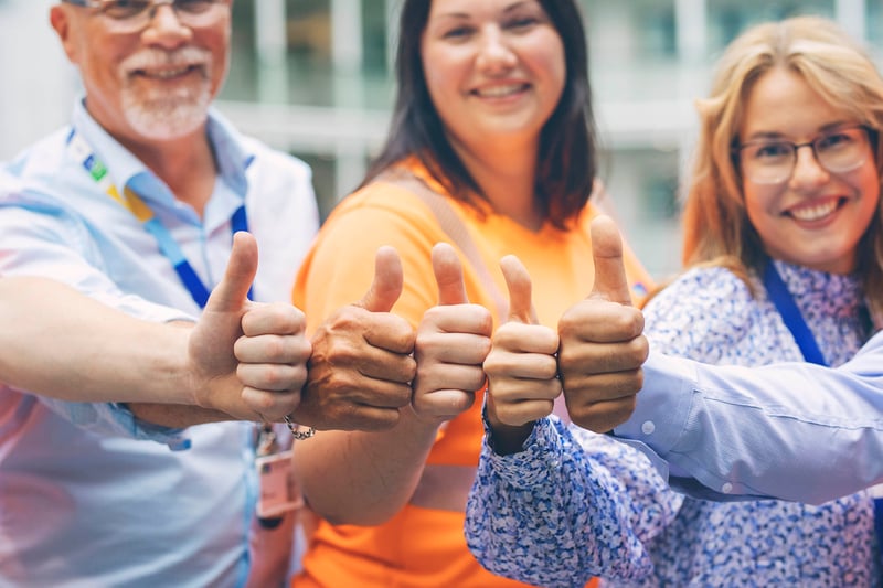 Kolme työkaverusta näyttävät peukaloa